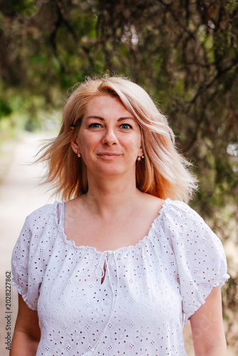 A portrait of a positive, charming, and cheerful woman on a walk. A blonde woman in a white blouse looks at us. The blonde has a determined look. 