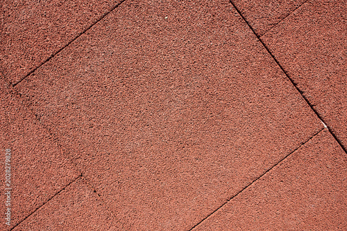 Outdoor daytime shot of an elastic terracotta safety playground tile surface exhibiting coarse granulation