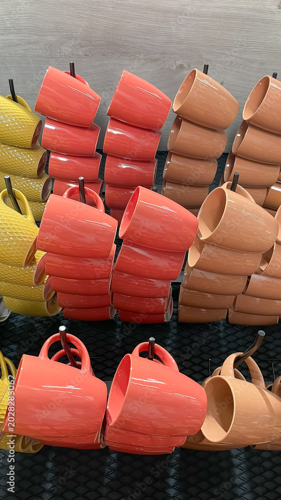 Fototapeta premium Neat retail display of colorful ceramic coffee mugs in orange yellow and beige shades stacked on hooks in a store