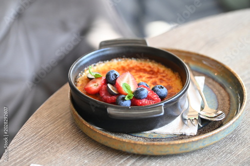 Fotografie French crème brûlée dessert with fresh fruit served in a black bowl