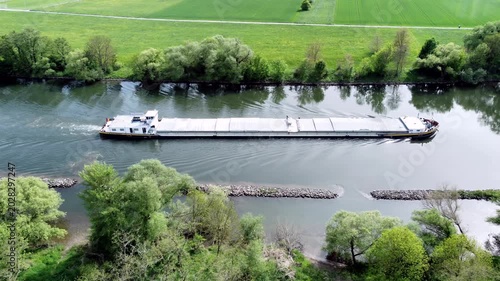 Drohne fliegt über Fluss mit Binnenschiff, Ufer mit Auwald und Agrarland, Luftaufnahme