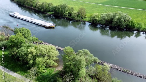 Drohne fliegt über Fluss mit Binnenschiff, Ufer mit Auwald und Agrarland, Luftaufnahme