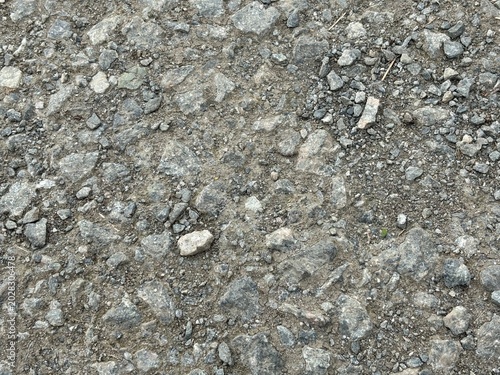 Close-up view of a rough asphalt surface, revealing the texture of embedded gravel and small stones, suggesting durability and urban landscapes.