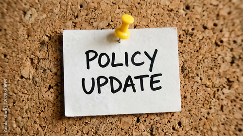 Policy Update handwritten note on white paper, corporate announcement pinned to cork board, business regulation change message with yellow pushpin