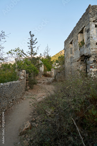Dirt walking path passing by ruined walls of abandoned old stone houses