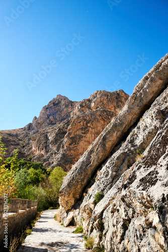 Sunlit steep angled rock formations along a deep gorge with green foliage