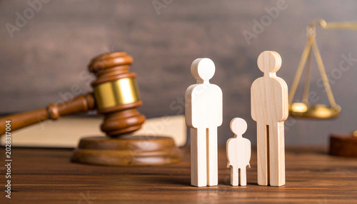 Wooden family figures stand on a desk with a blurred judge's gavel, law books, and scales of justice, representing family disputes and legal protection