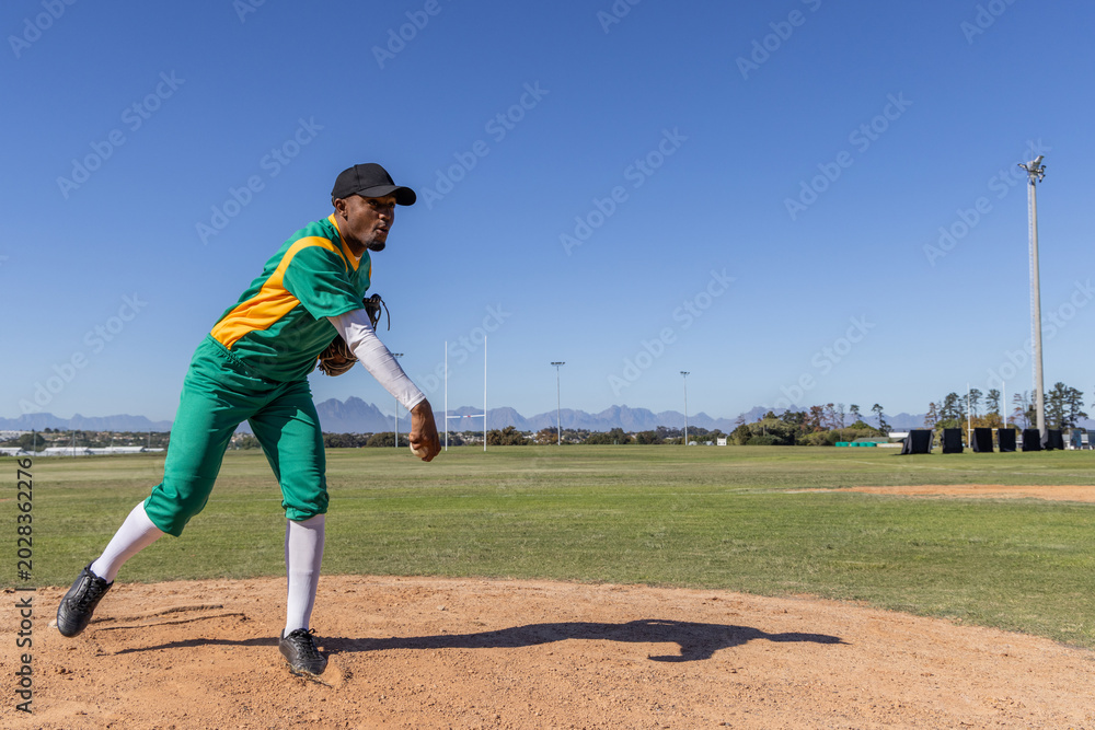 Obraz premium African American man pitching on dirt mound at field wearing green uniform and glove, copy space