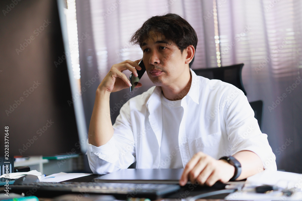 Fototapeta premium Asian man taking an important phone call, concentrating on the conversation and working from his home office, managing business remotely, communicating ideas and solutions