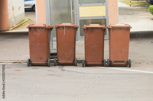 Row of brown garbage and recycling bins standing on a city street, urban waste management concept, municipal sanitation and everyday residential infrastructure outdoors.