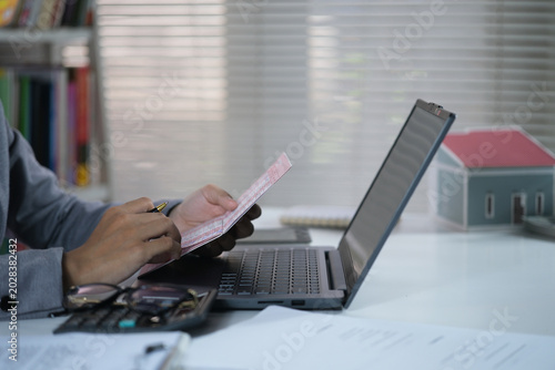 Obraz na płótnie Open and check the printout of savings book, view bank account book in front of laptop, account statement, check payment and income, financial documents, pay slip, cash balance, investment, business
