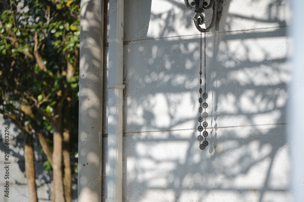 Obraz premium Metal decorative chain hanging from building edge casting sharp shadow on white wall, US Military Housing, Yangmingshan, Shilin District, Taipei, Taiwan, strong afternoon directional sunlight.