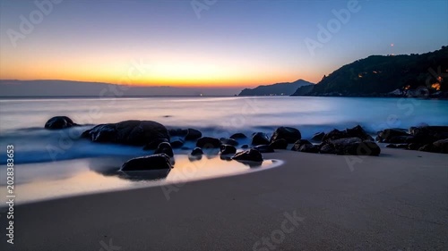 Seaside twilight scene features a calm beach, rocks in the water, and colorful horizon