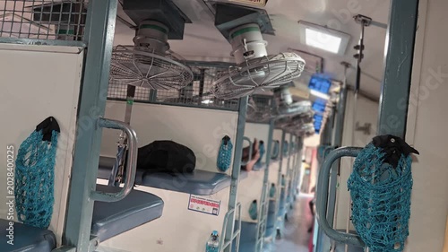 Sleeper coach interior of Indian Railways with blue berths for sleep and leisure. Metal ceiling fans & blue mesh bottle holders on frames offer pure comfort, encouraging quiet relaxation and deep rest