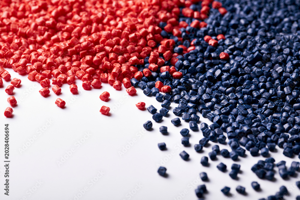 Fototapeta premium High-angle close-up shot of vibrant red and deep blue industrial plastic pellets scattered on a clean white background, showcasing raw materials for polymer manufacturing and chemical processing.