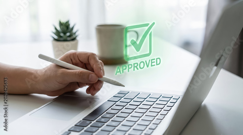 Closeup of a person using a digital pen on a laptop with a glowing green approved checkmark icon overlay