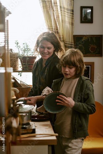 Fotografia Vertical shot of Caucasian mother and child washing dishes together in home kitchen, sharing household routine and family teamwork