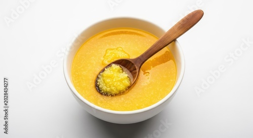 Golden homemade pure traditional ghee in a white ceramic bowl with a rustic wooden spoon on top, isolated on a clean white background, cooking, healthy, lactose-free