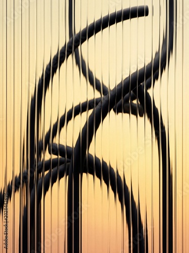 Abstract black metal structures warp behind textured fluted glass against a warm sunset gradient