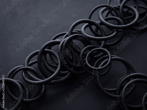 Black rubber o-ring gaskets arranged in overlapping patterns on a dark textured background
