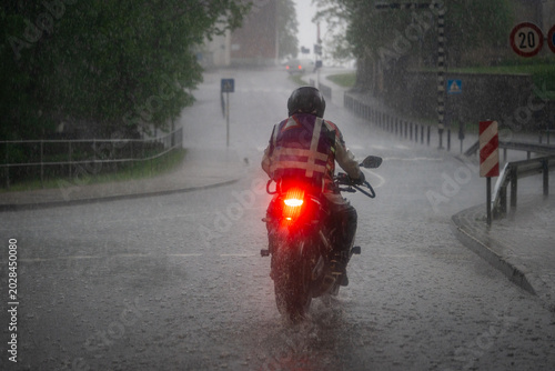 Motorcyclist riding through heavy rainstorm on flooded urban street during extreme weather