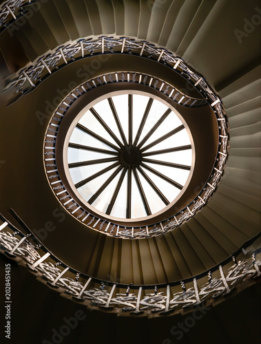 Looking up into the Tulip Stairs reveals a hypnotic vortex of timeless beauty. A central, wheel-like skylight casts a radiant, ethereal glow over the inner rings. This light fades into deep, dramatic 