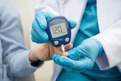 Foto Asian doctor using digital glucose meter for check sample blood sugar level to treatment diabetes