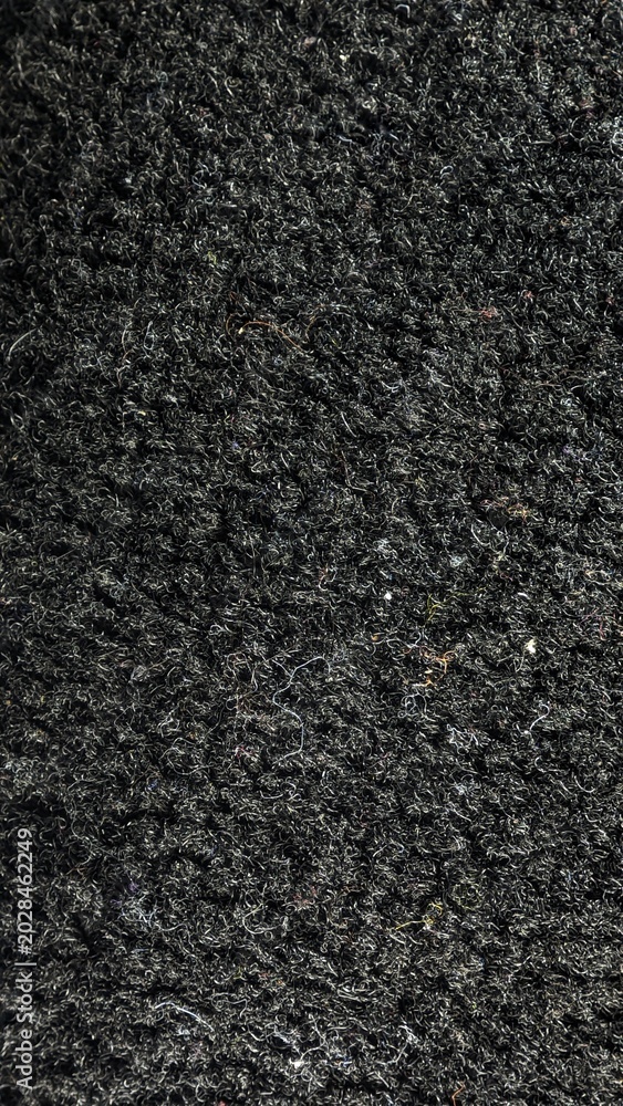 Fototapeta premium Vertical close-up texture of dark black rough woven carpet fabric background.