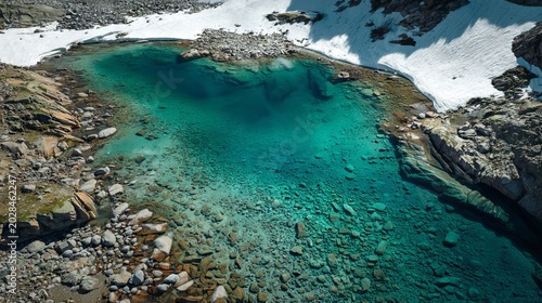 Aerial view of a glacial lake with clear turquoise water surrounded by rocks and patches of snow