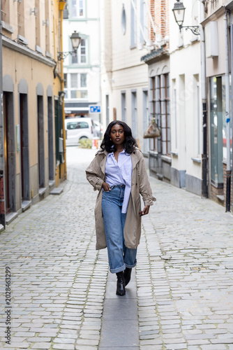 Tableau sur toile Confident young woman walking down historic cobblestone street in European city