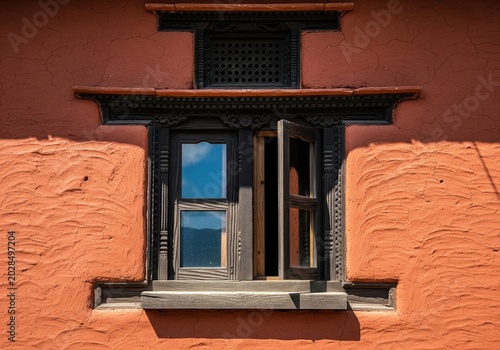 Open wooden window with dark carved frame on textured red clay wall of traditional house