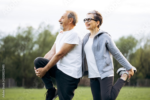 Canvas Print Mature couple warming up with leg stretches outdoors, achieving fitness goals an