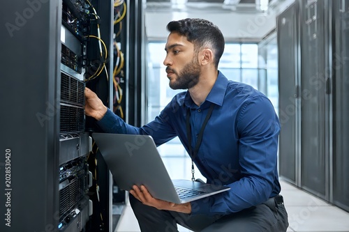 IT Engineer Monitoring Server Systems with Laptop in Modern Data Center