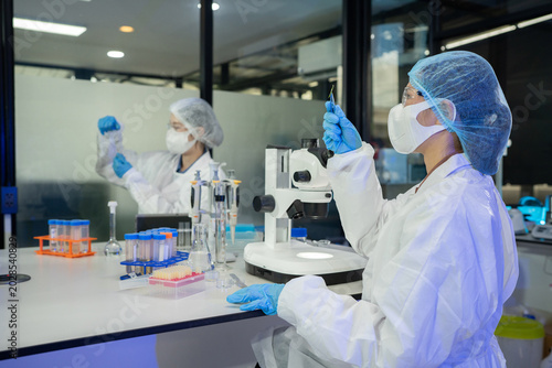 Photos Two lab technicians wearing white coats, masks, and gloves analyze specimens bes