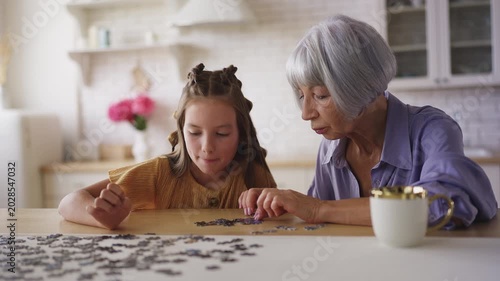 Adorable girl and her granny solving jigsaw puzzle together, family pastime