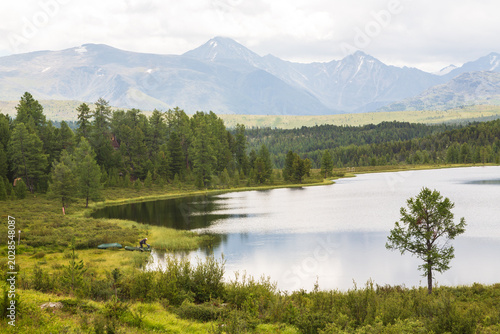  A figure of a fisherman in a boat and a picturesque Lake Kodelyukyol in Ulagan region in summer in Altai. Ulagan, Altai, Siberia, Russia