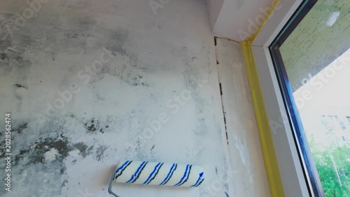 Person rolling primer over interior wall near window during renovation