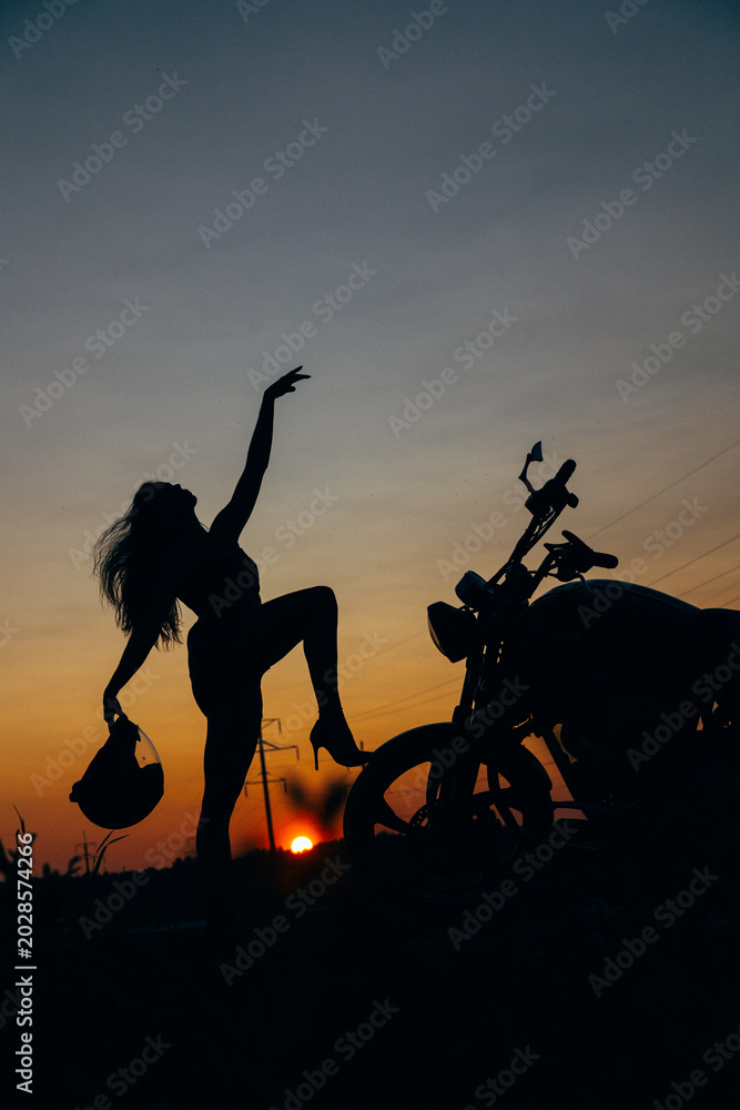 Fototapeta premium Silhouette of Woman with Motorcycle at Sunset Sky