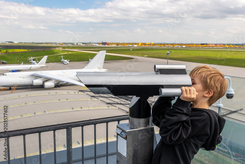 Foto Curious little kid boy watching aircraft through observation telescope at Leipzig airport panorama terrace