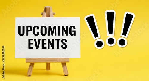 Upcoming events text on white board, wooden easel stand on yellow background, announcement and schedule concept with exclamation marks