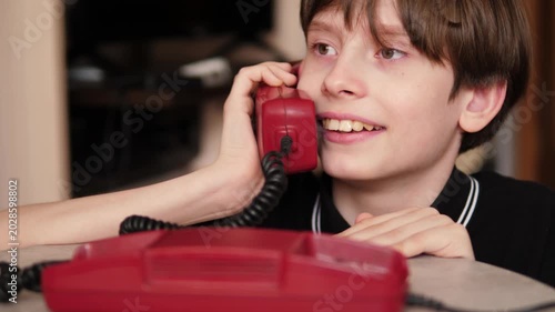 A happy boy smiles joyfully and quickly picks up the receiver of a landline red retro telephone. The child enthusiastically starts a phone conversation on the vintage device 