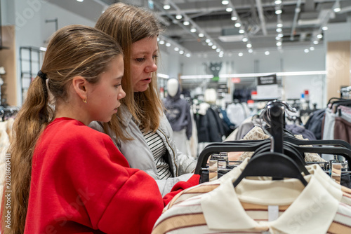 Tableau sur toile Focused mother and daughter meticulously examine clothing items on rack in brightly lit retail store, sharing moment of thoughtful fashion selection