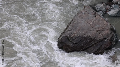 Large boulder standing in turbulent rushing mountain river water