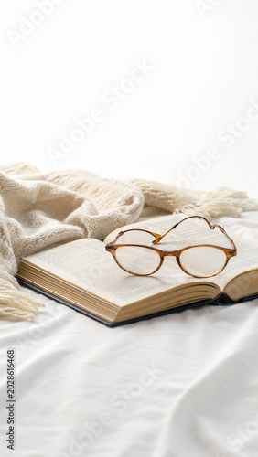 Quiet Reading Retreat: A soft knit throw blanket rests beside an open vintage book, paired with classic glasses to evoke a serene atmosphere of cozy relaxation and intellectual comfort.