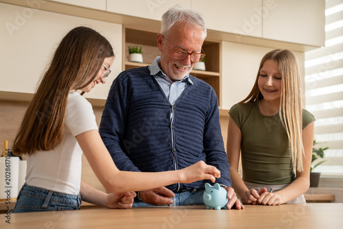 Fotografie Grandfather saving money with granddaughters and piggy bank at home