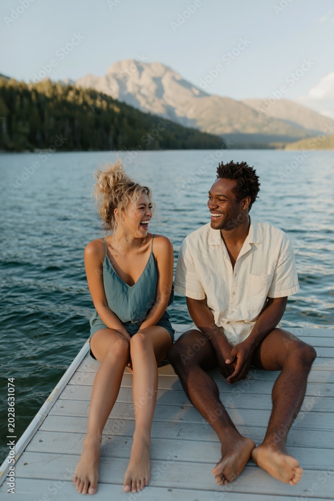 Fototapeta premium Young couple laughing together on dock by mountain lake