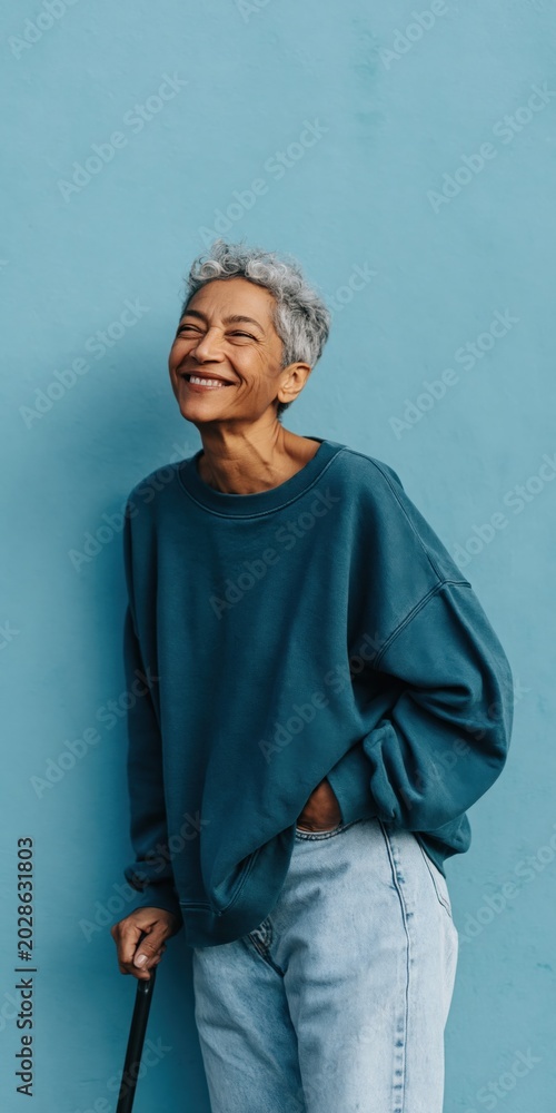 Obraz premium Older woman laughing while holding cane against blue wall