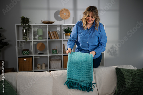Fotografía Woman tidying living room folding turquoise blanket