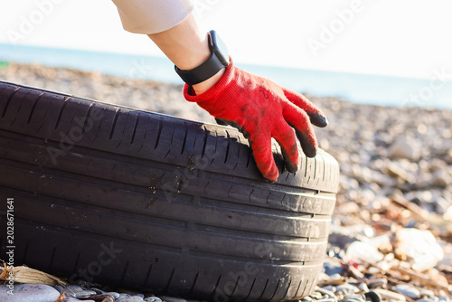 Foto Hand in red glove grips discarded tire on shore