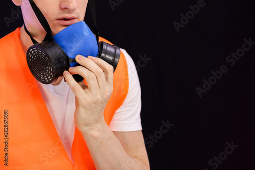 Hand adjusting strap on blue respirator mask worn with orange vest